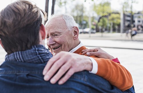 Smiling senior man looking at adult grandson outdoors